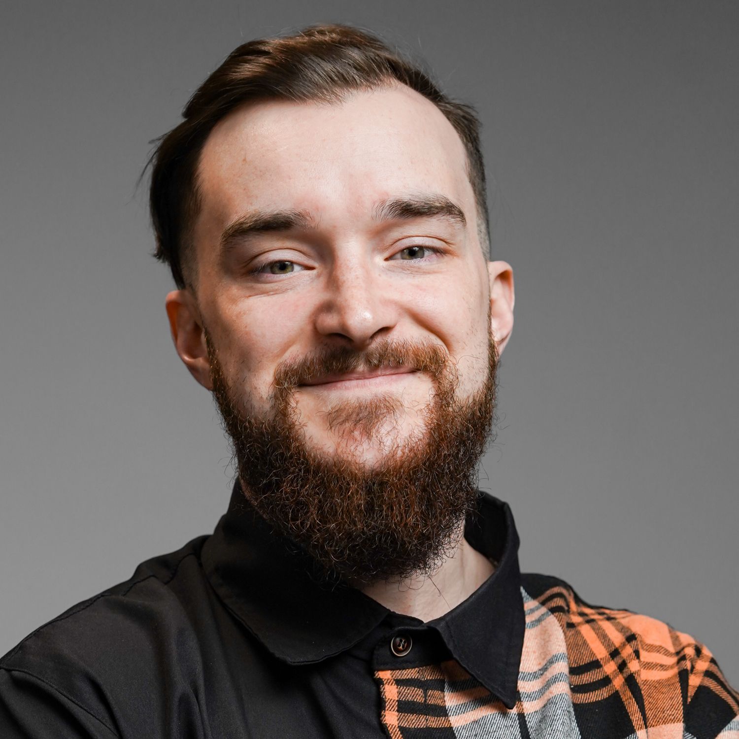 A man with a beard is wearing a plaid shirt and smiling for the camera.