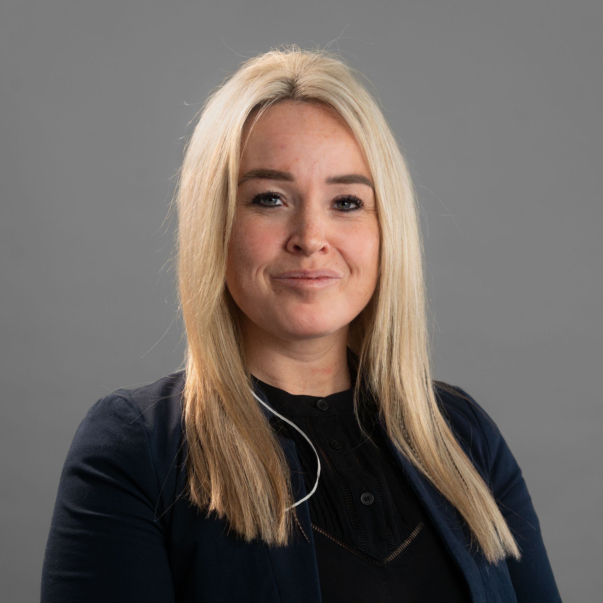 A woman with blonde hair is wearing a black shirt and a blue jacket.