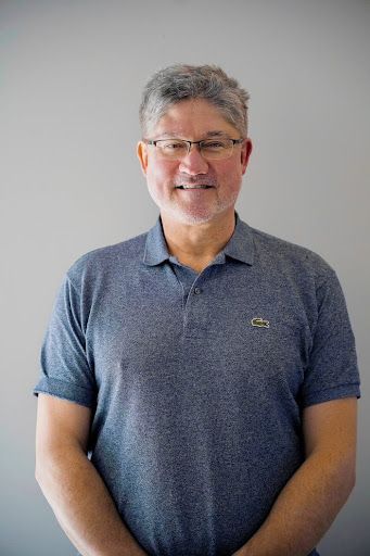 A man with a beard and glasses is wearing a blue polo shirt.