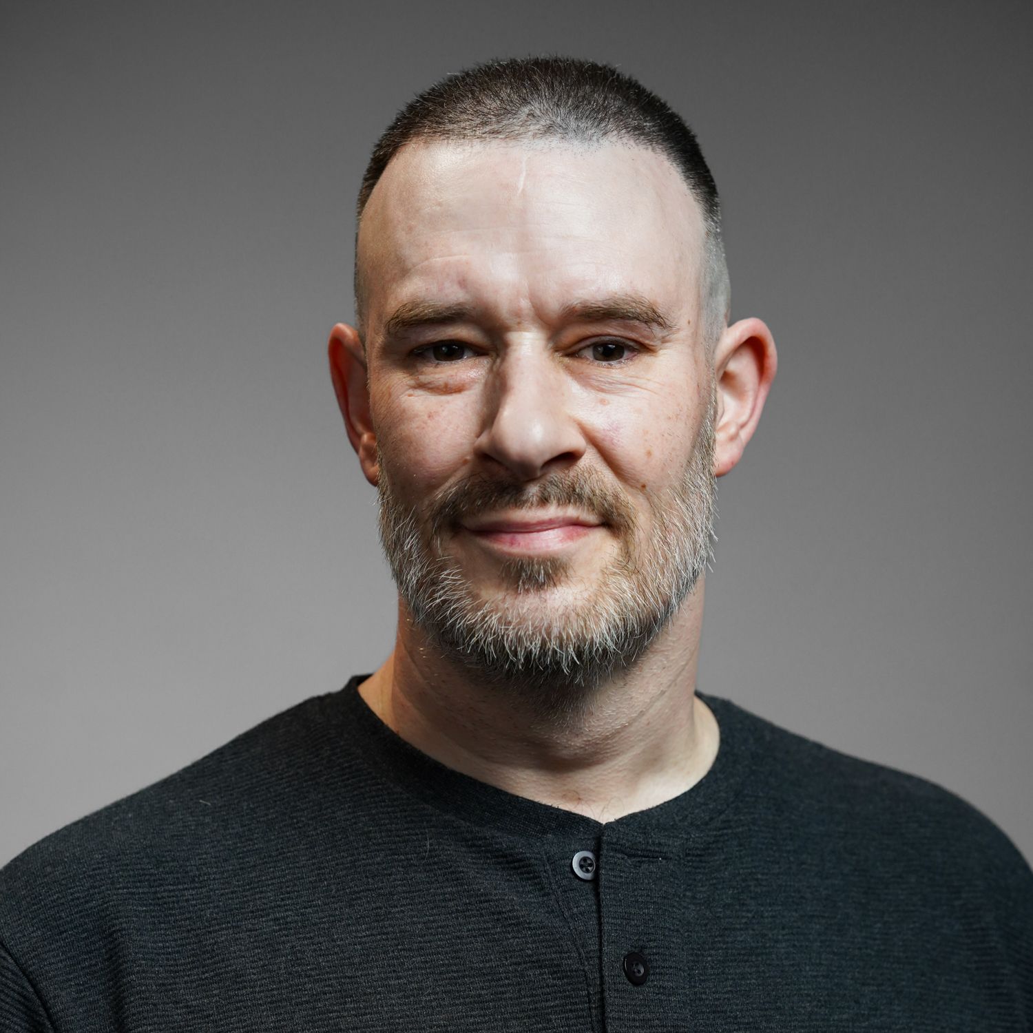 A man with a beard is wearing a black shirt and smiling for the camera.