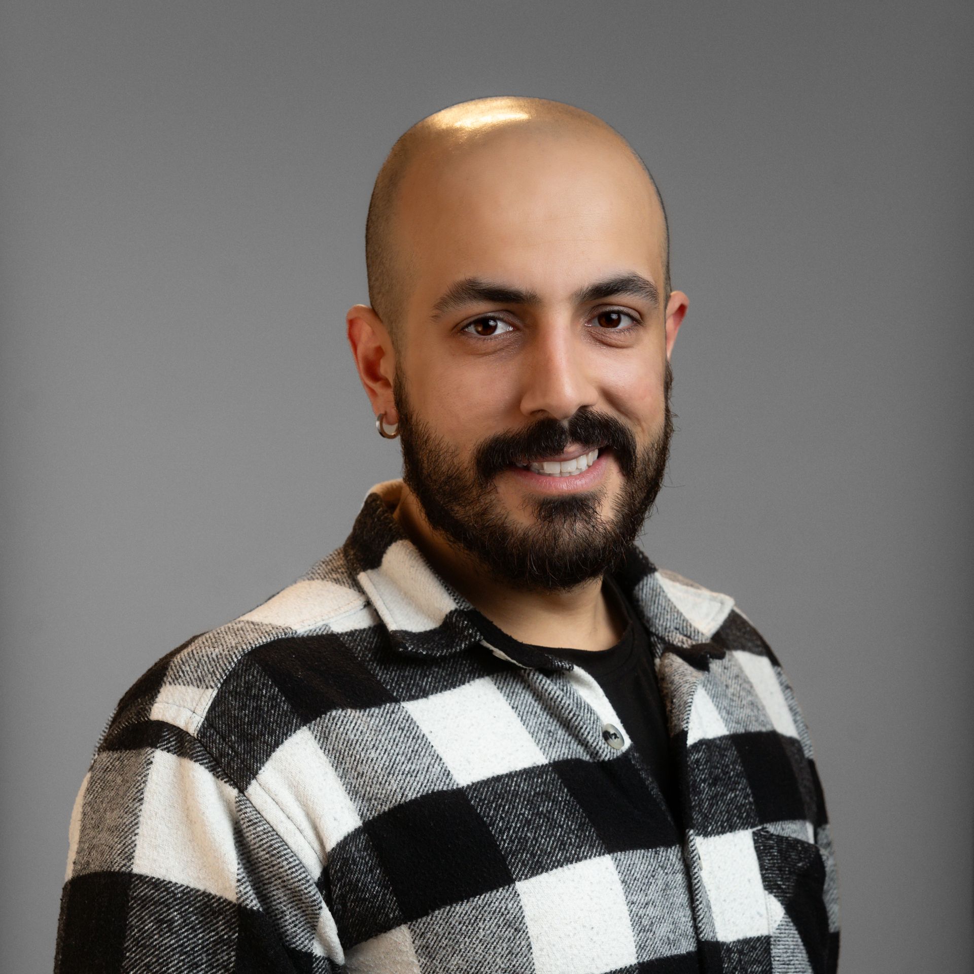A bald man with a beard is wearing a black and white plaid shirt.