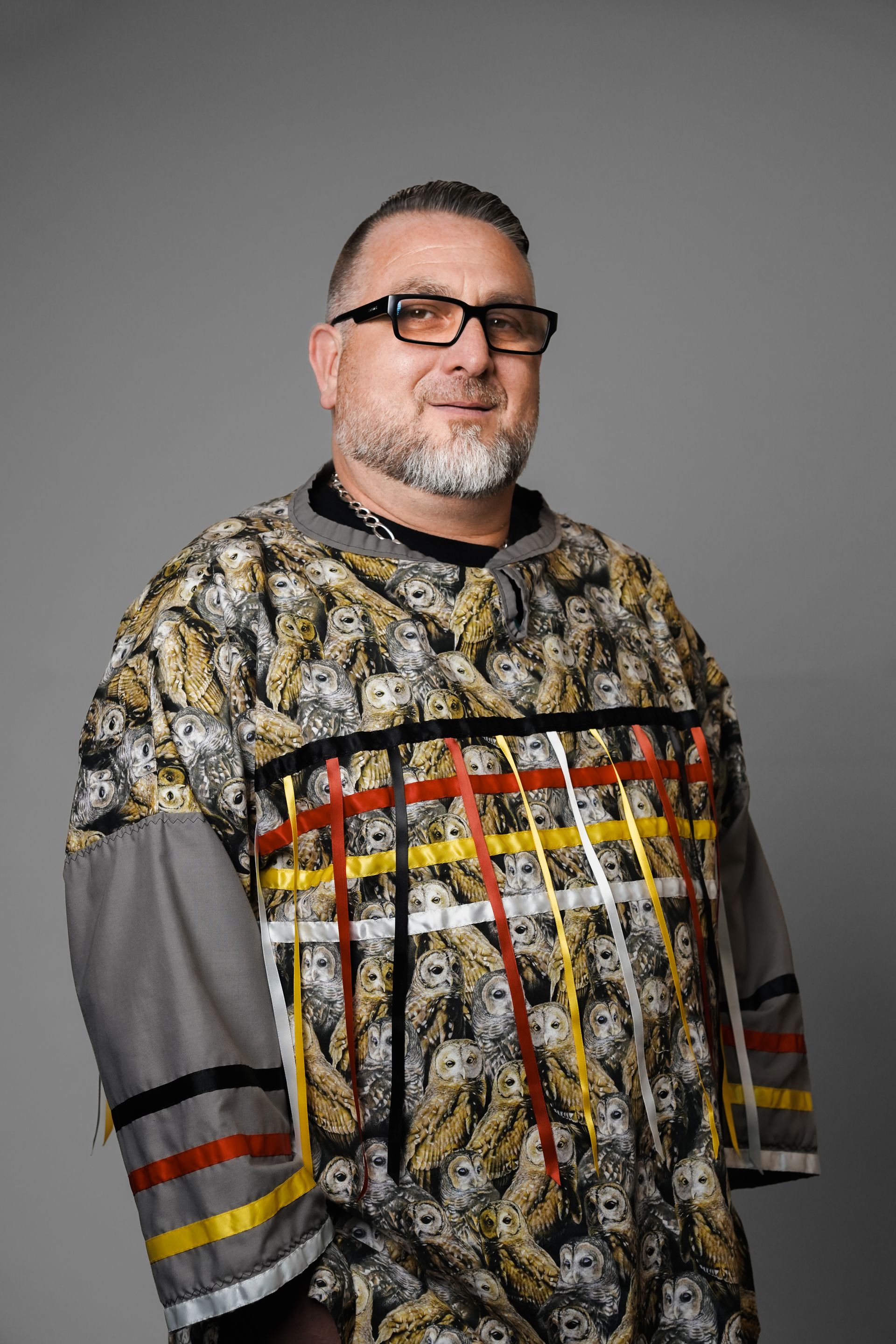 A man with a beard and glasses is wearing a colorful shirt.