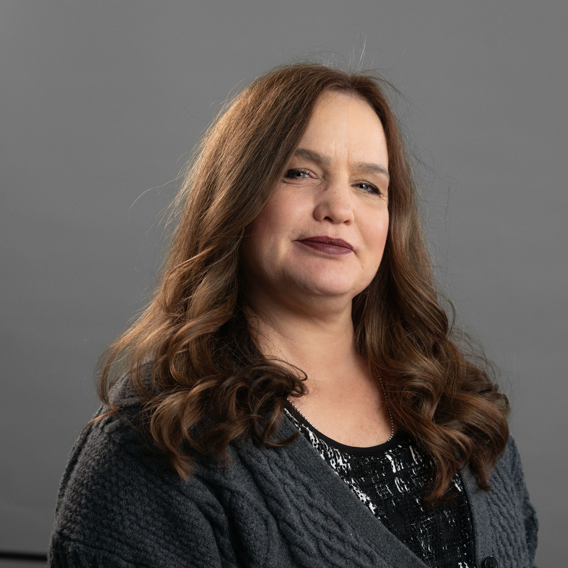A woman with long brown hair is wearing a gray sweater and a black top.