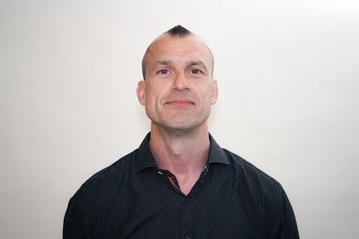 A man in a black shirt is standing in front of a white wall.