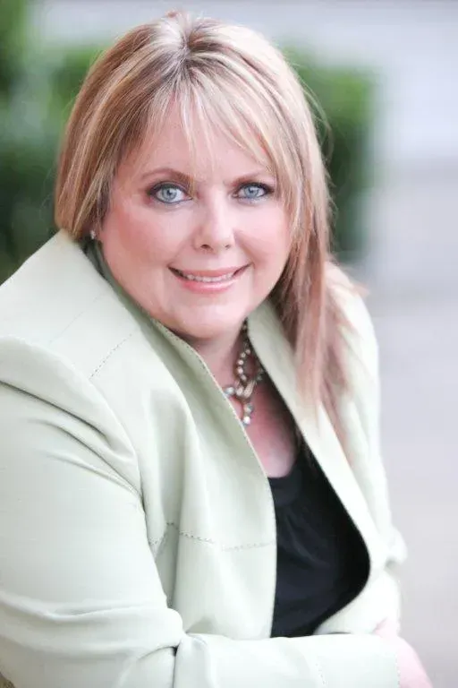 A woman in a green jacket and black shirt is smiling for the camera.