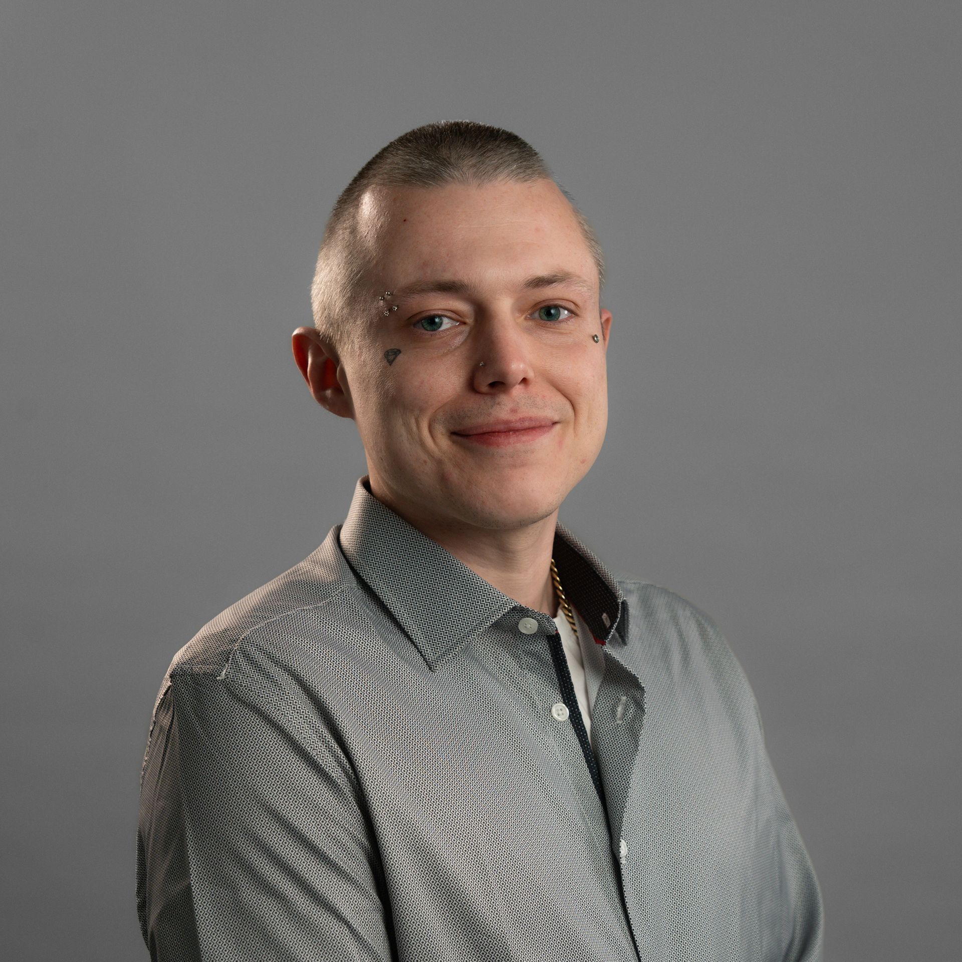 A man with a tattoo on his face is smiling and wearing a gray shirt.