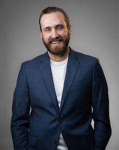 A man with a beard is wearing a blue suit and smiling.