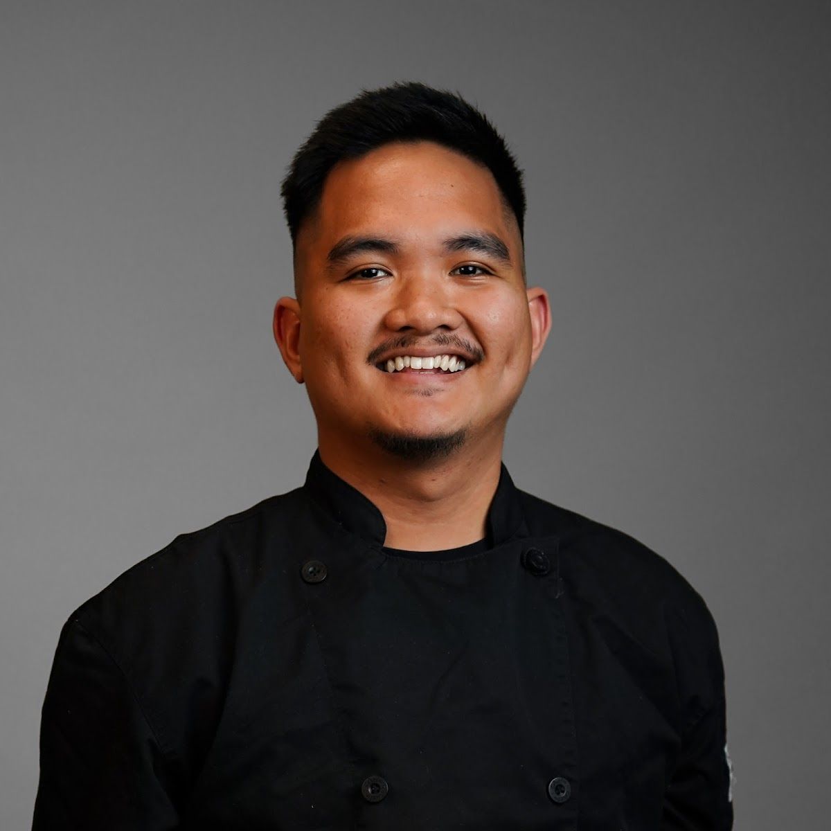 A man in a chef 's uniform is smiling for the camera