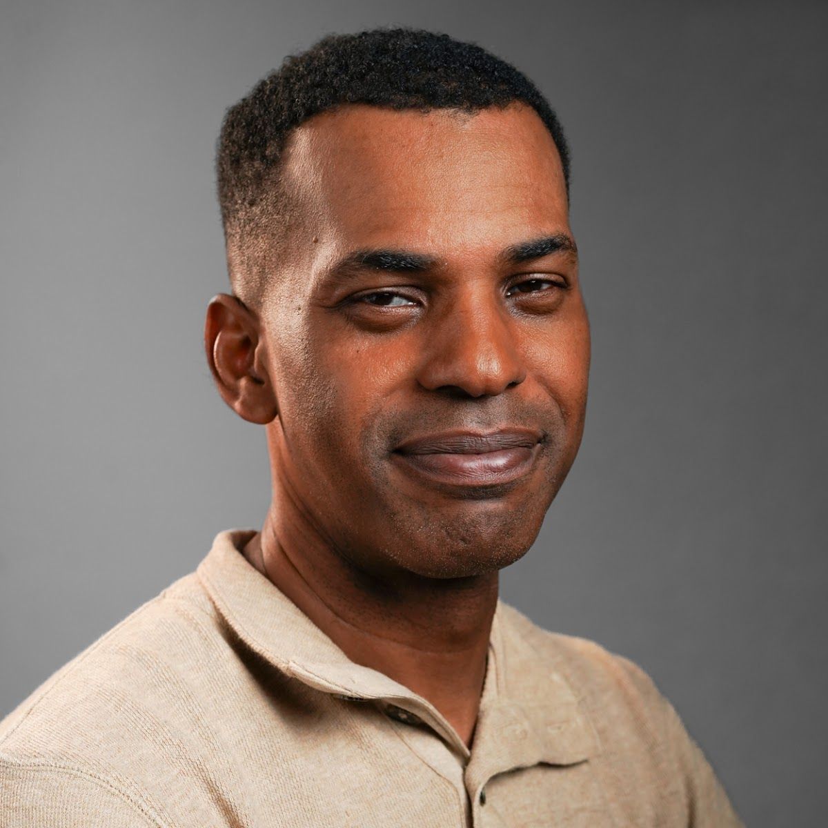 A man in a tan shirt is smiling for the camera