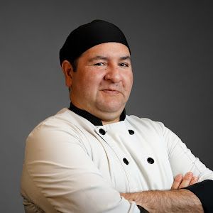 A man in a chef 's uniform is standing with his arms crossed.