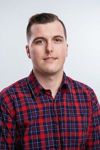 A young man wearing a red and blue plaid shirt is looking at the camera.