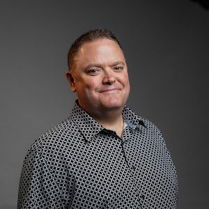 A man in a black and white shirt is smiling for the camera.