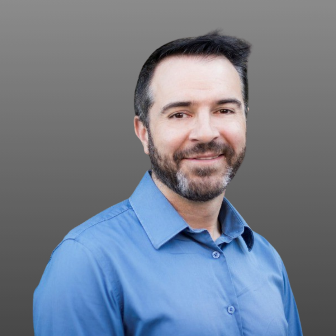 A man with a beard is wearing a blue shirt and smiling.