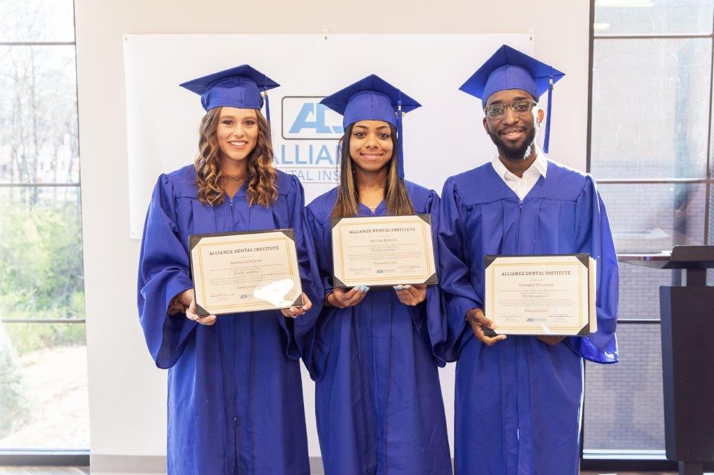 Three graduates in blue caps and gowns holding diplomas.