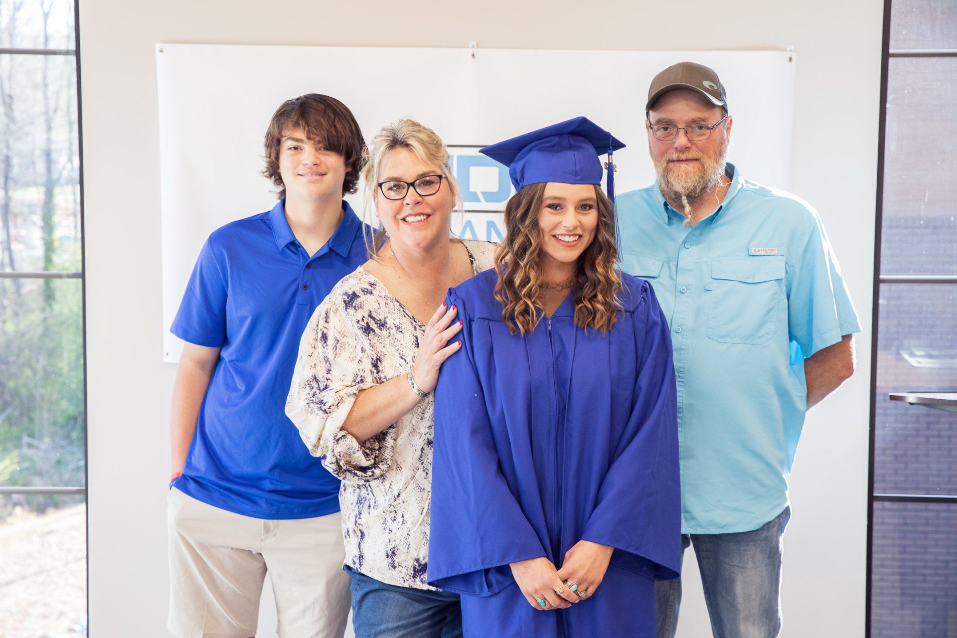 Family posing for a graduation photo; a graduate in blue gown, family in blue, white, and tan, neutral background.