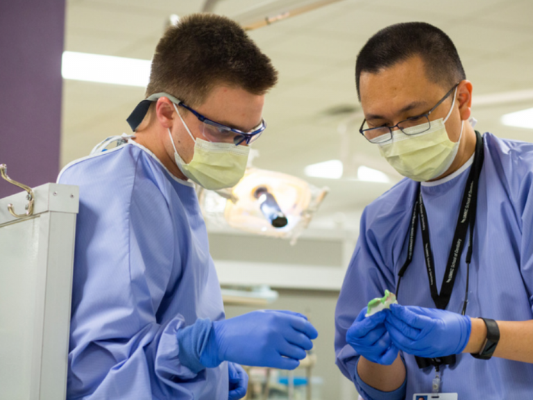 Two men wearing masks and gloves are working in a lab.