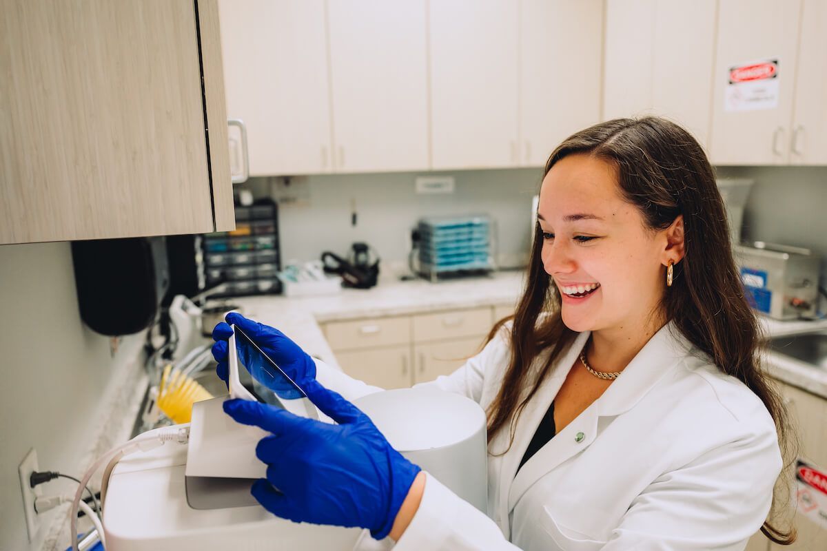 A woman in a lab coat and blue gloves is working in a lab.