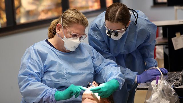 Two female dentists are examining a patient 's teeth in a dental office.