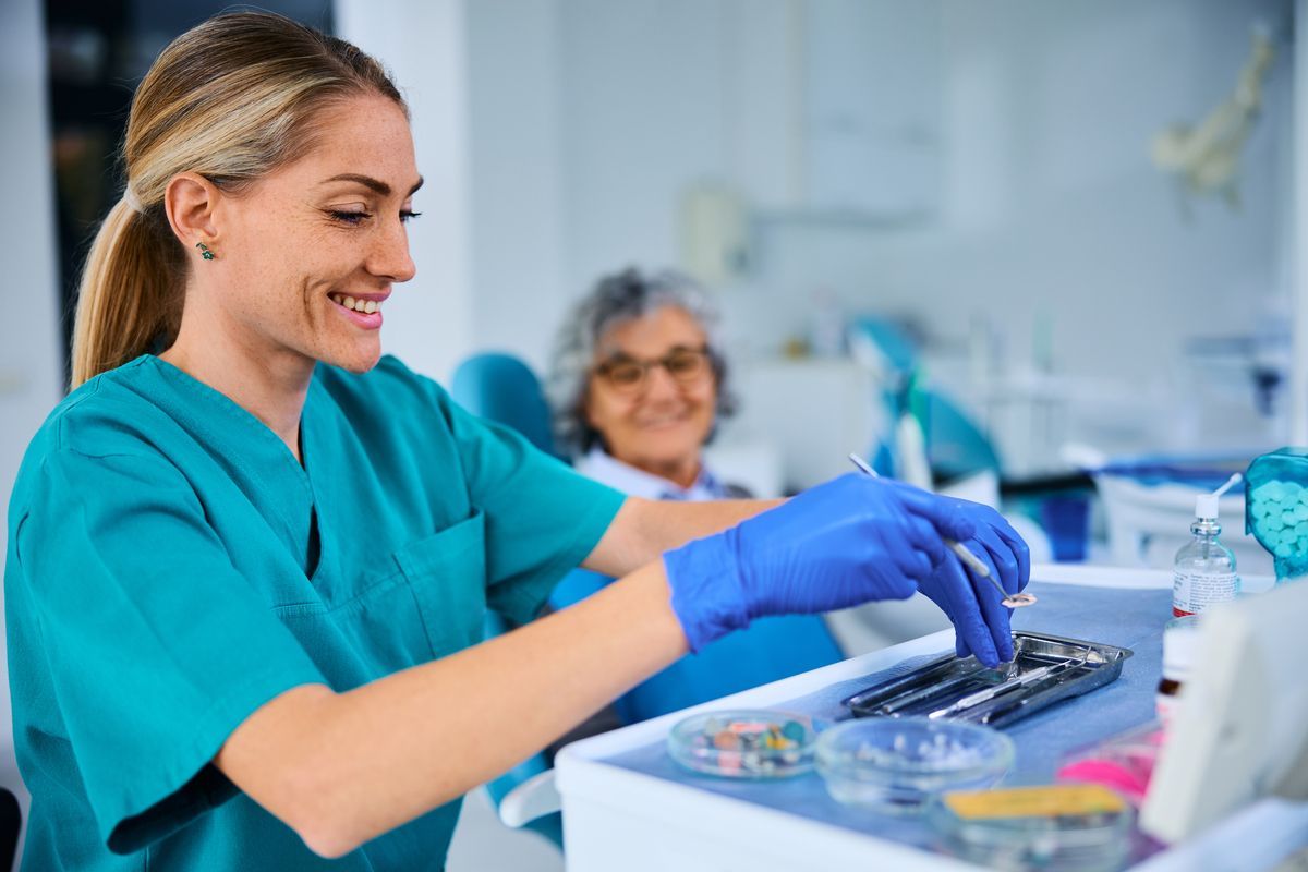 Dental assistant  in teal scrubs and gloves handling dental tools