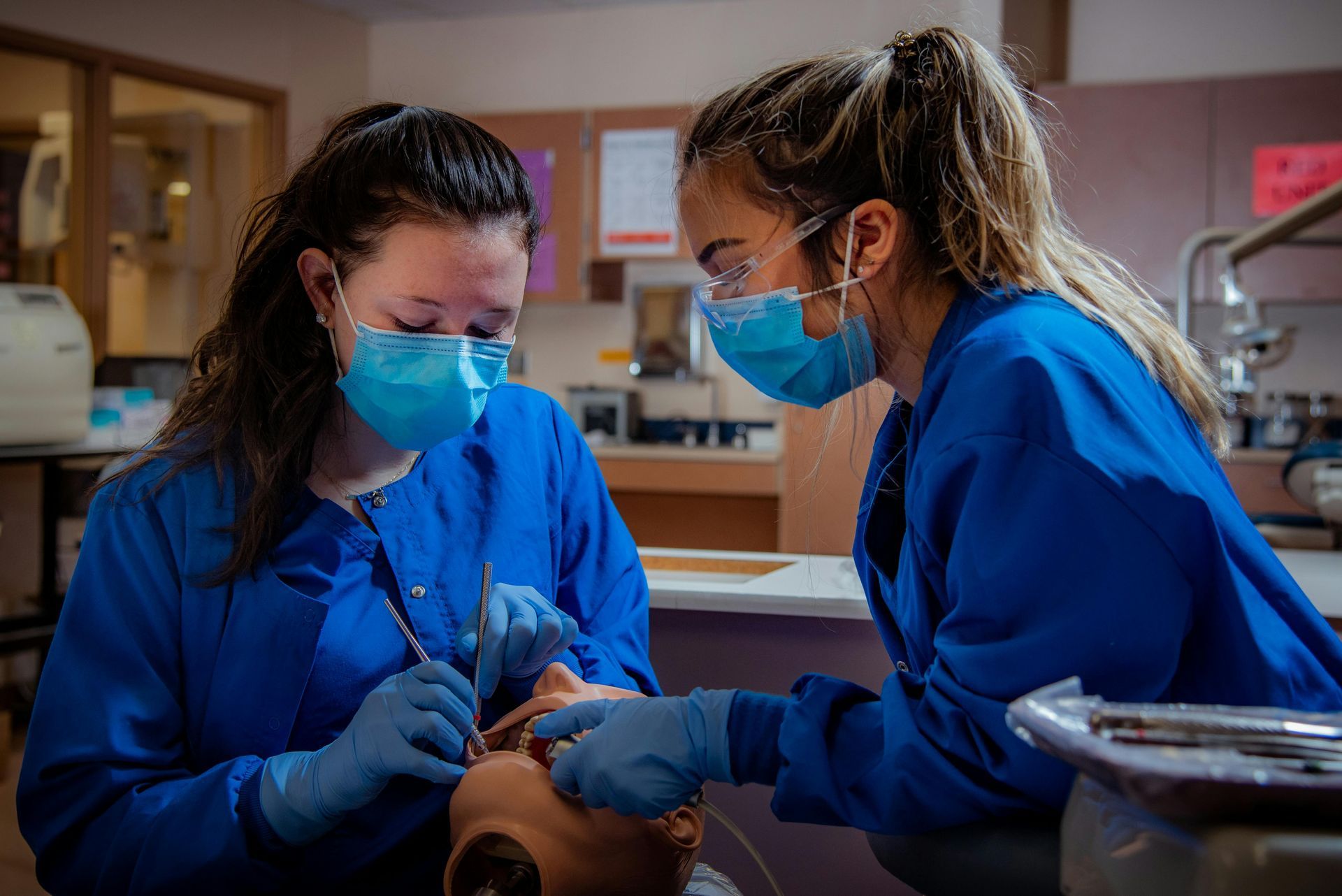 Two female dentists are working on a mannequin in a dental office.