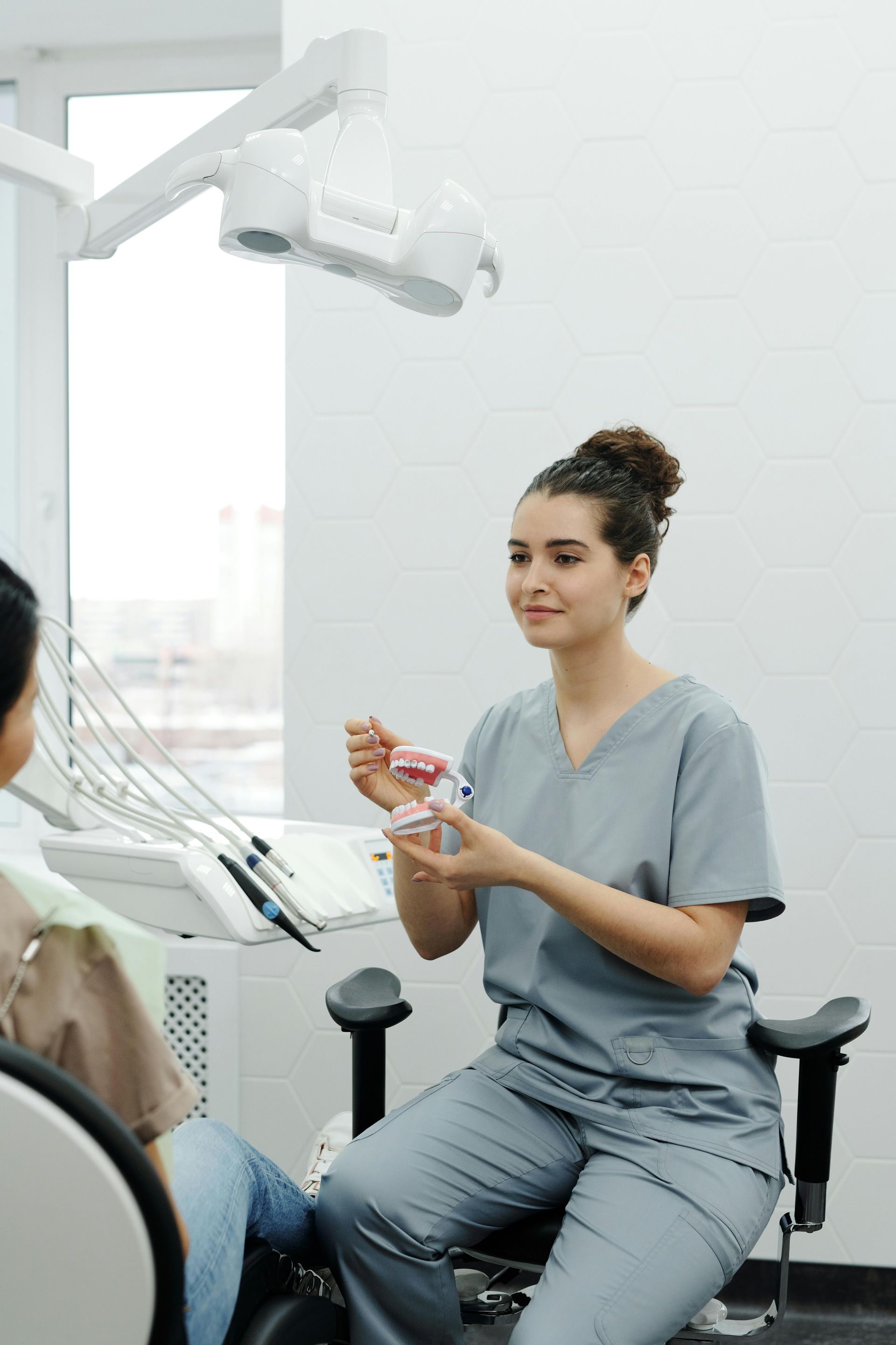 A female dentist is sitting in a dental chair talking to a patient.