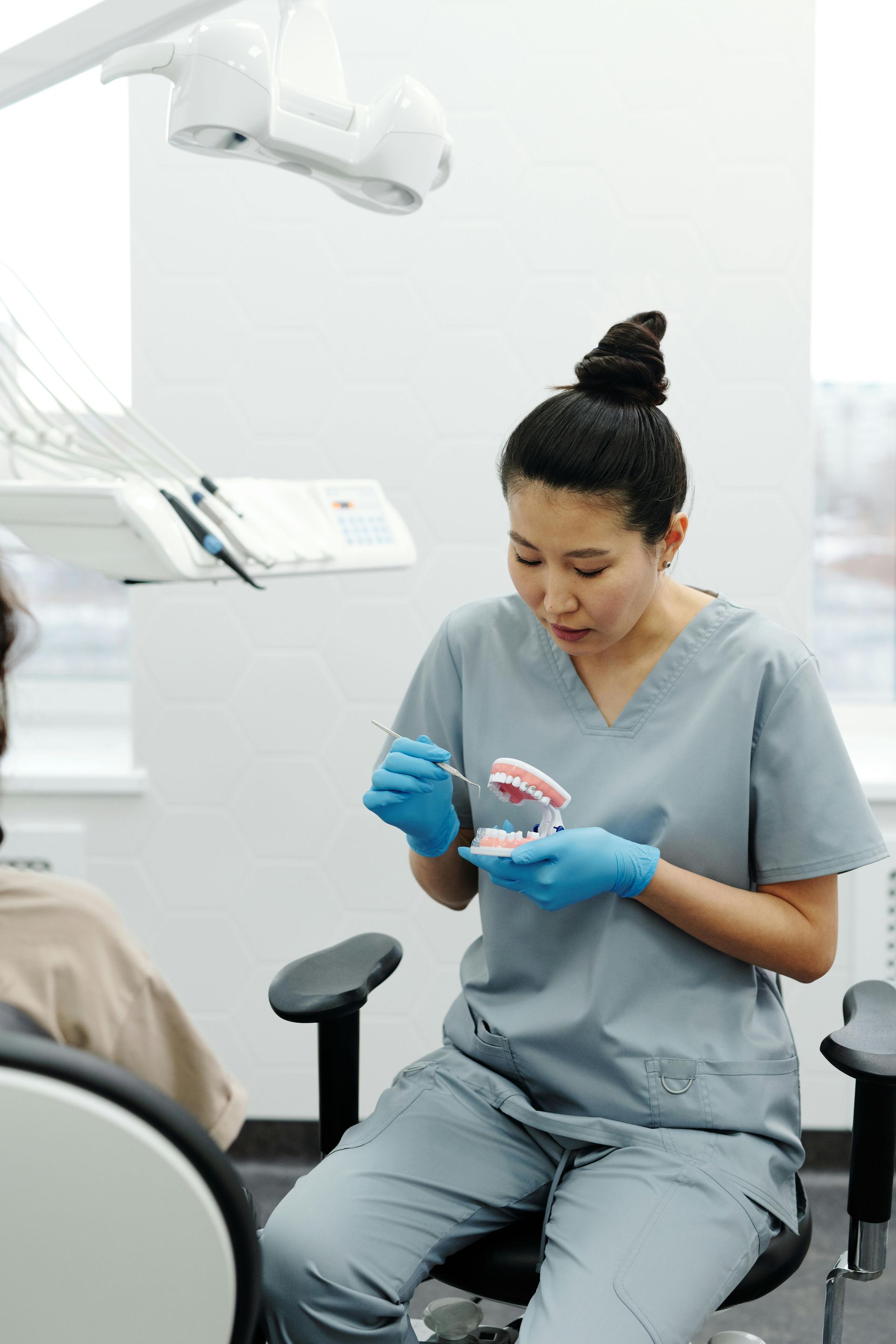 Dentist in scrubs, showing a dental model, in an examination room.