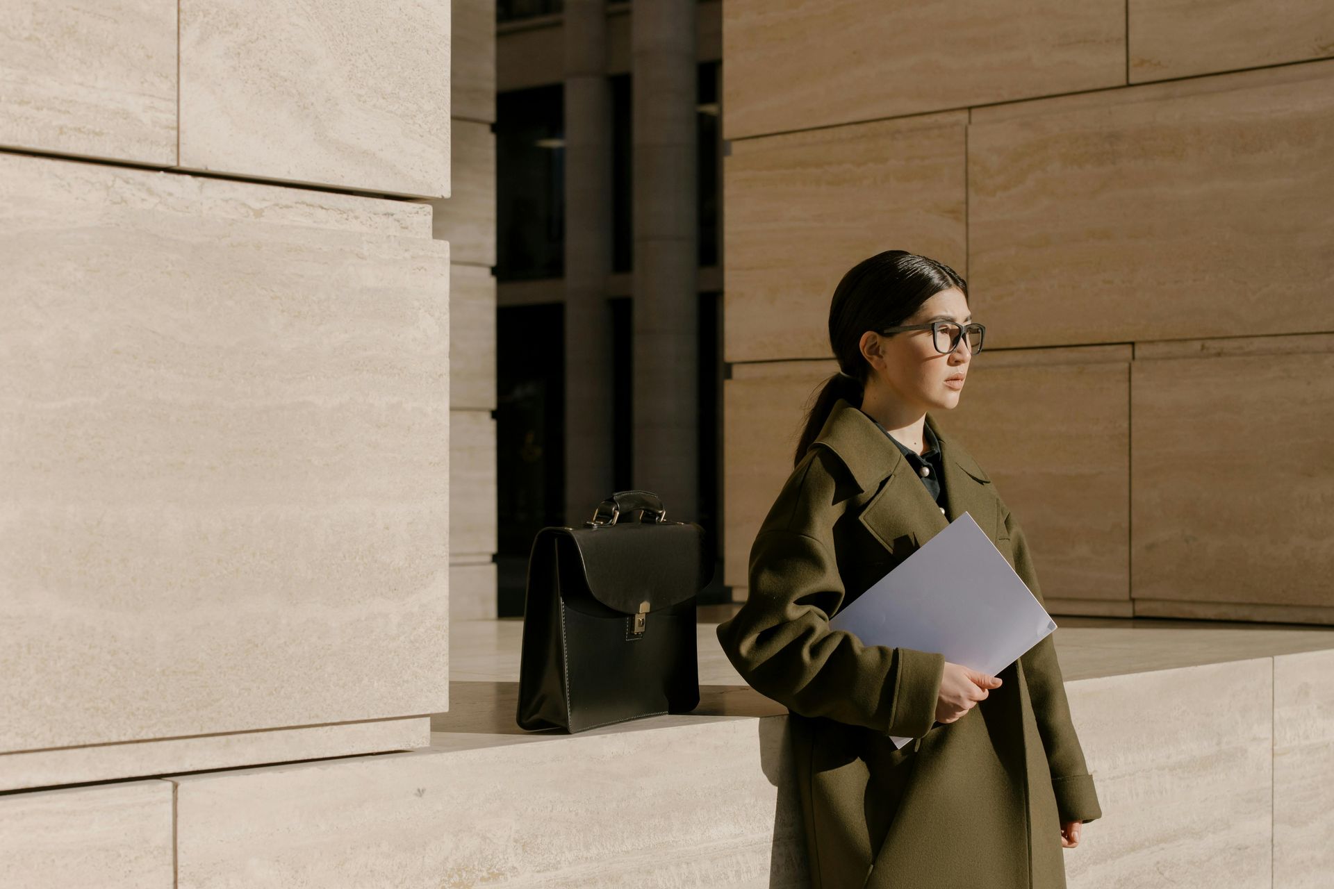 A woman in a trench coat is holding a piece of paper and a briefcase.