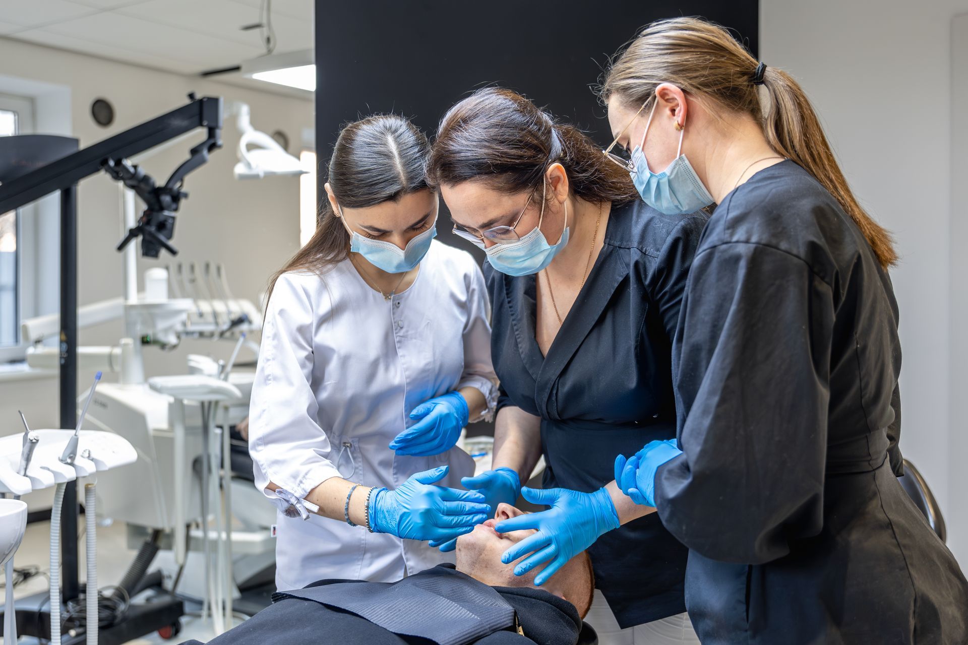 Three dental professionals wearing masks and blue gloves examine a patient in a medical office.