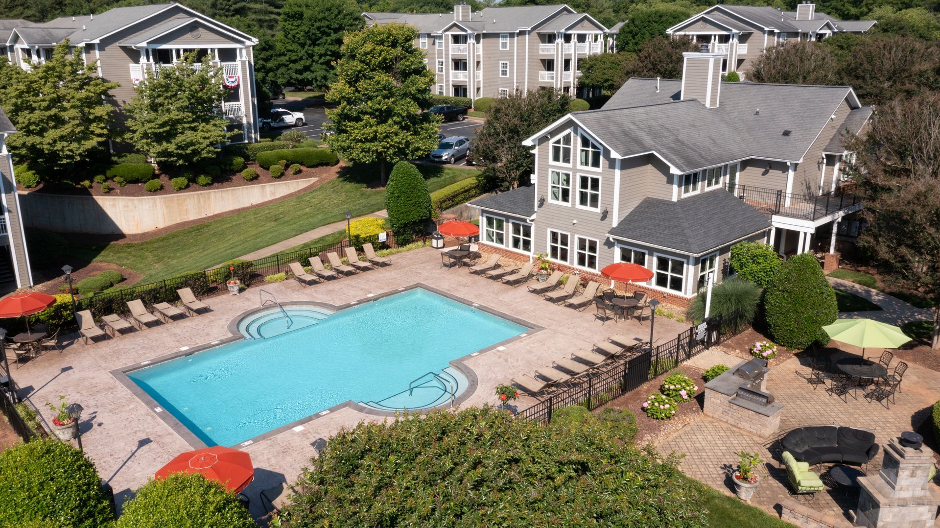 Aerial view of an apartment complex with a pool, lounge chairs, and a clubhouse.