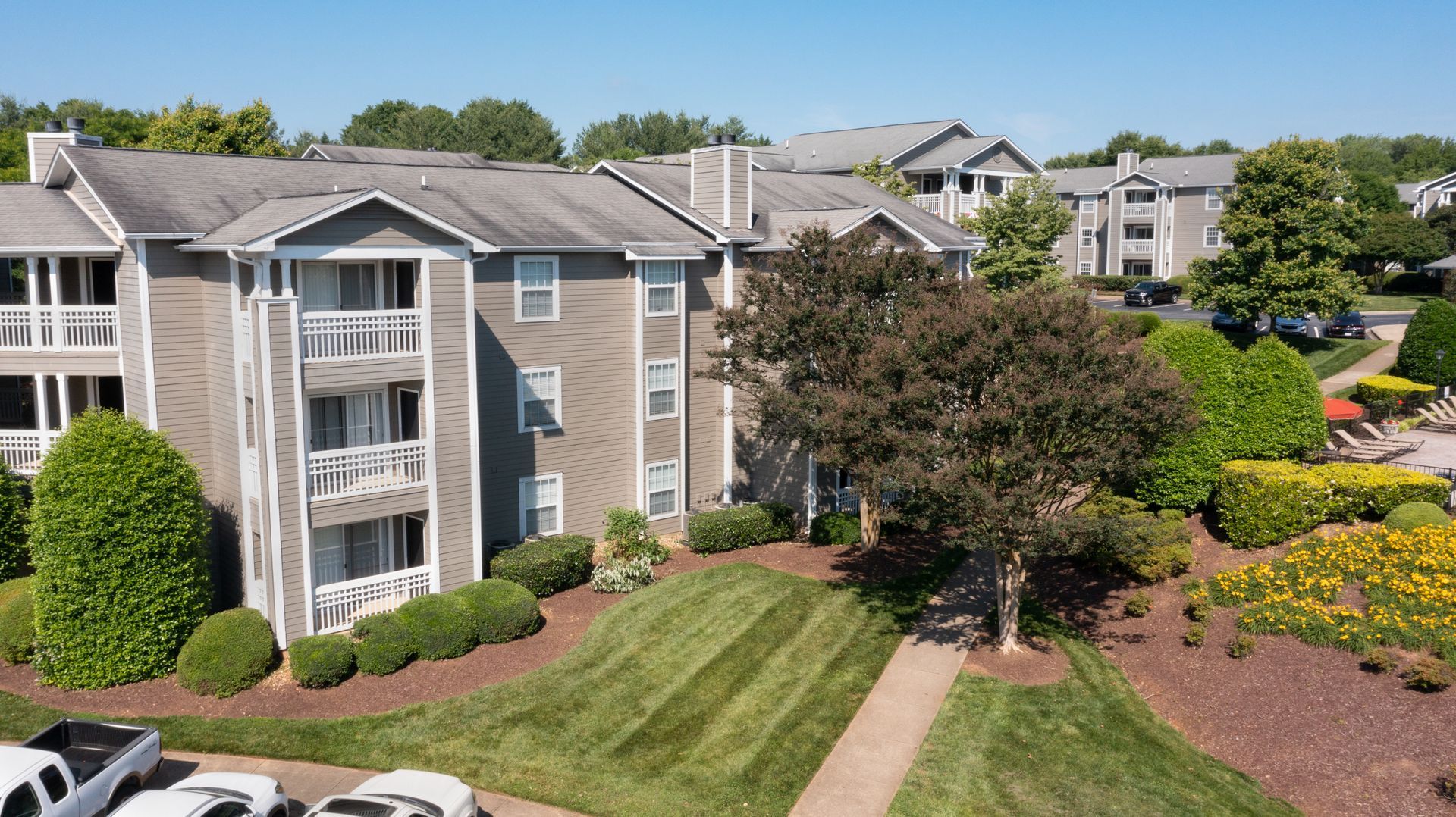 Apartment complex with balconies and a green lawn under a sunny sky.