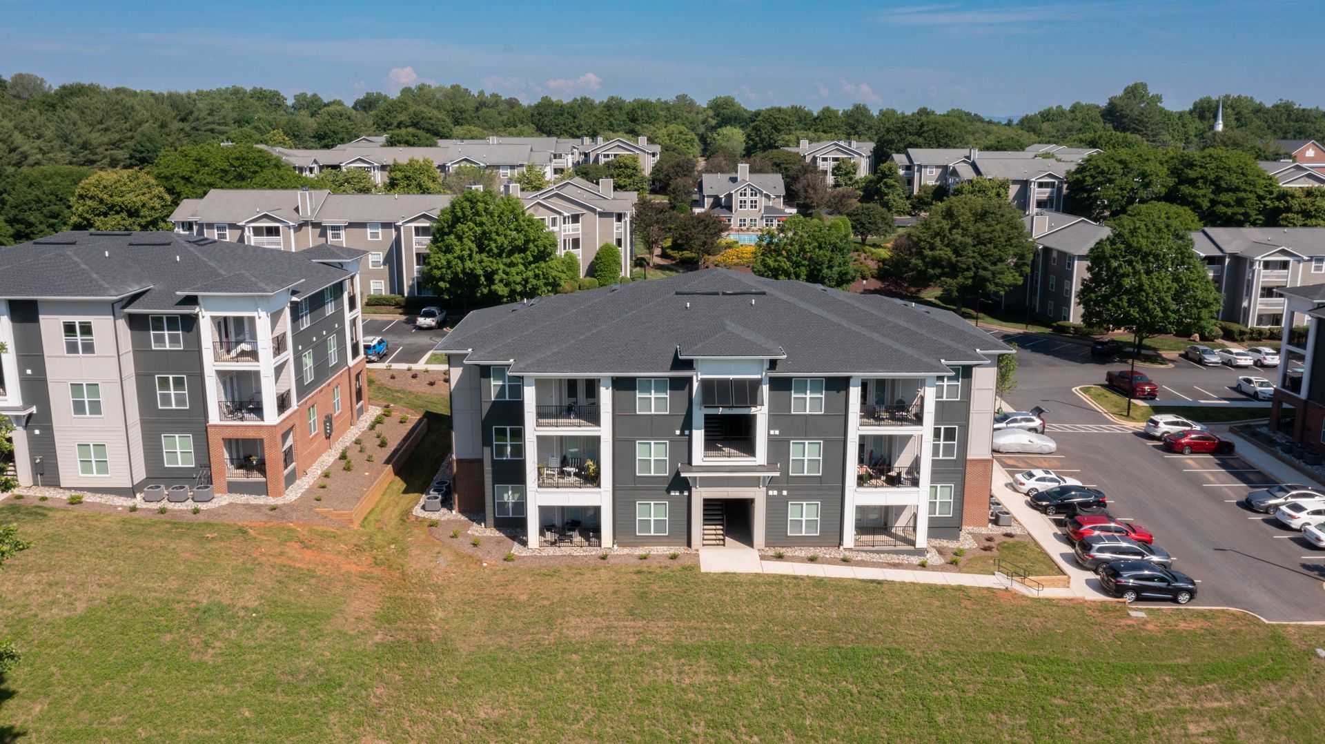 Aerial view of apartment complex with gray buildings, green lawn, and parked cars. Blue sky.