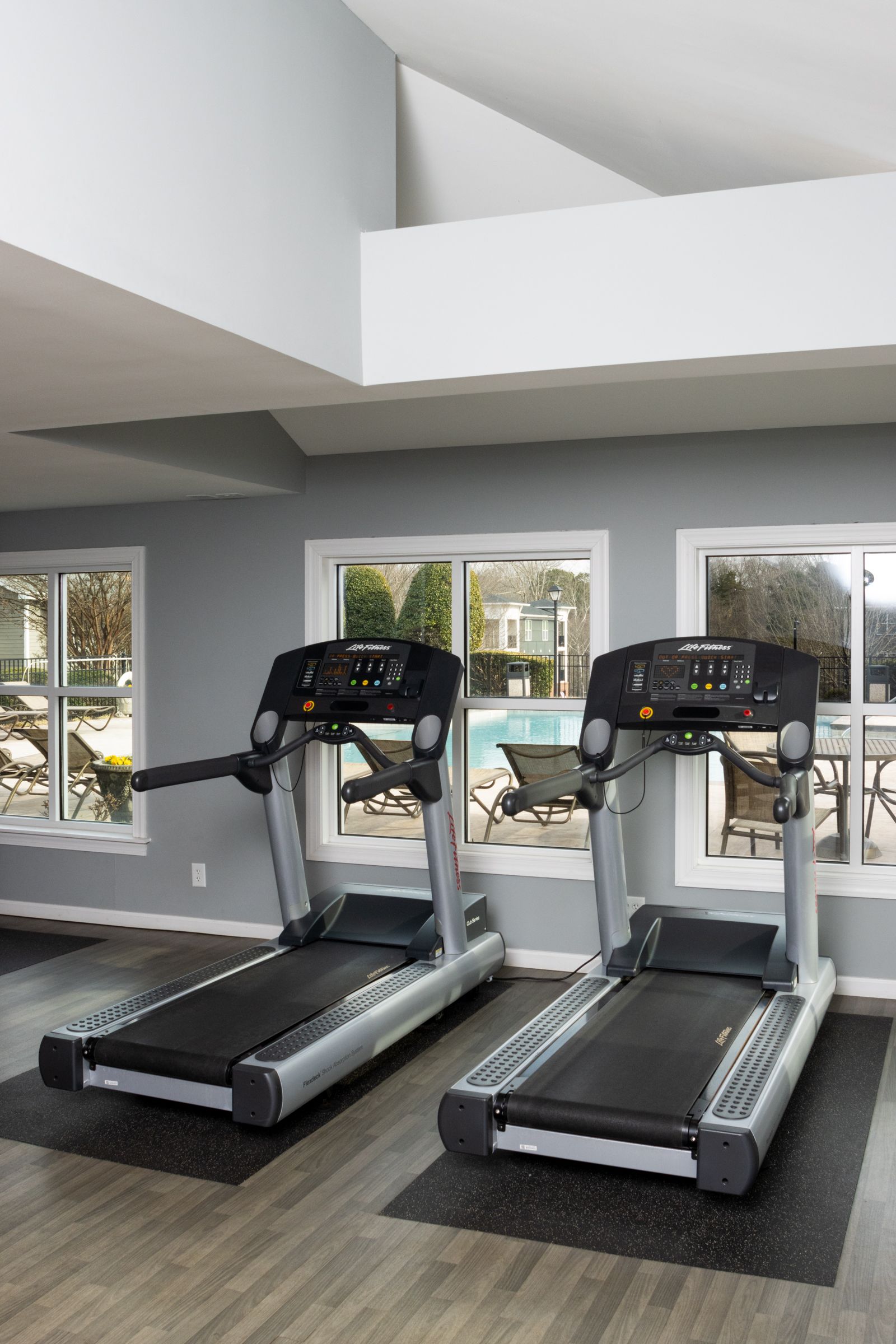 Two treadmills in a gym setting with windows overlooking a pool.