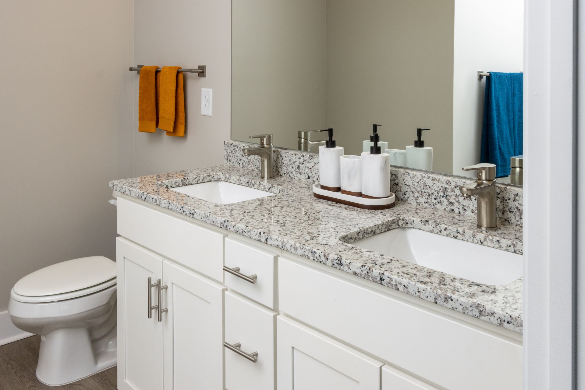 Bathroom with white double vanity, granite countertop, two sinks, and a toilet.