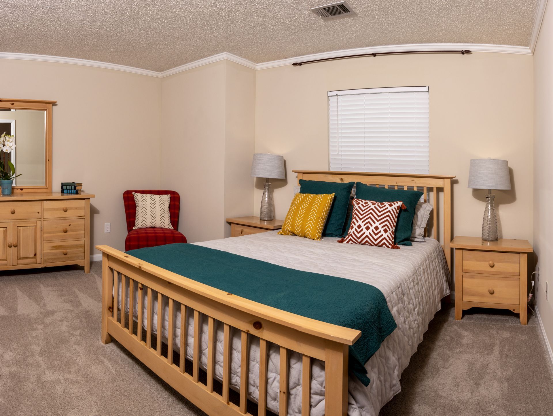 Bedroom with light wood furniture, bed with teal throw, two nightstands, and a red chair.