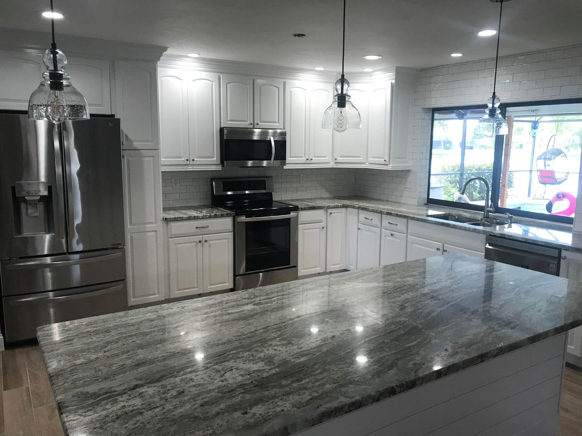 A kitchen with white cabinets , granite counter tops , stainless steel appliances and a large island.