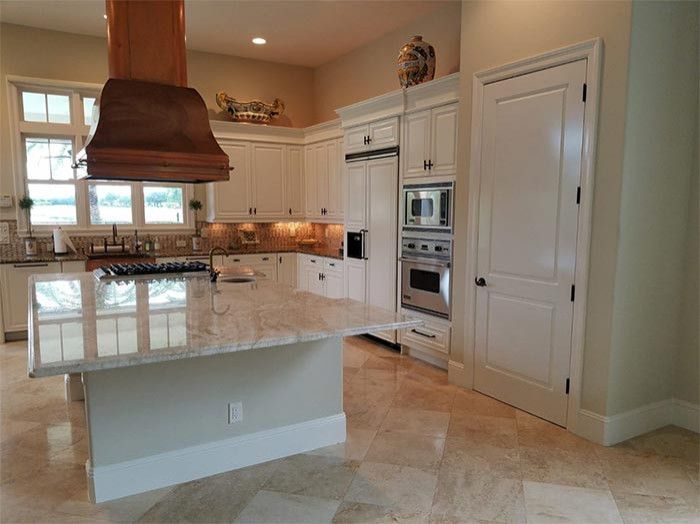 A kitchen with white cabinets , granite counter tops , stainless steel appliances and a large island.