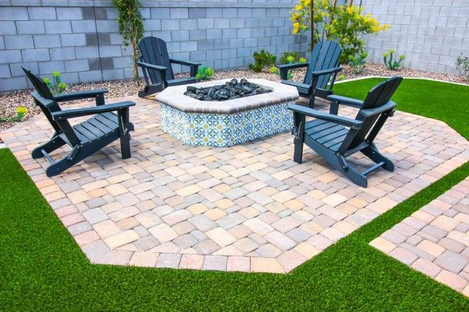 Four dark wooden chairs surround an octagonal tiled fire pit on a stone paver patio set within a lawn area.