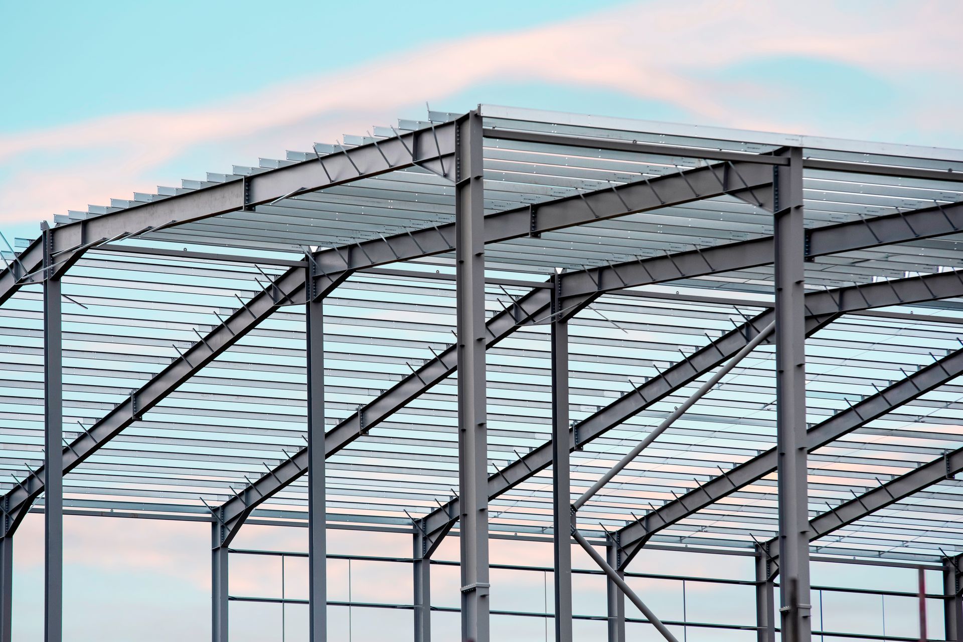 Steel framework of a building under construction, against a blue and pink sky.