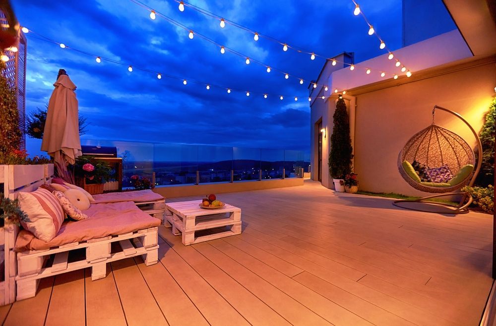 A patio with chairs , tables , umbrellas and string lights at night.