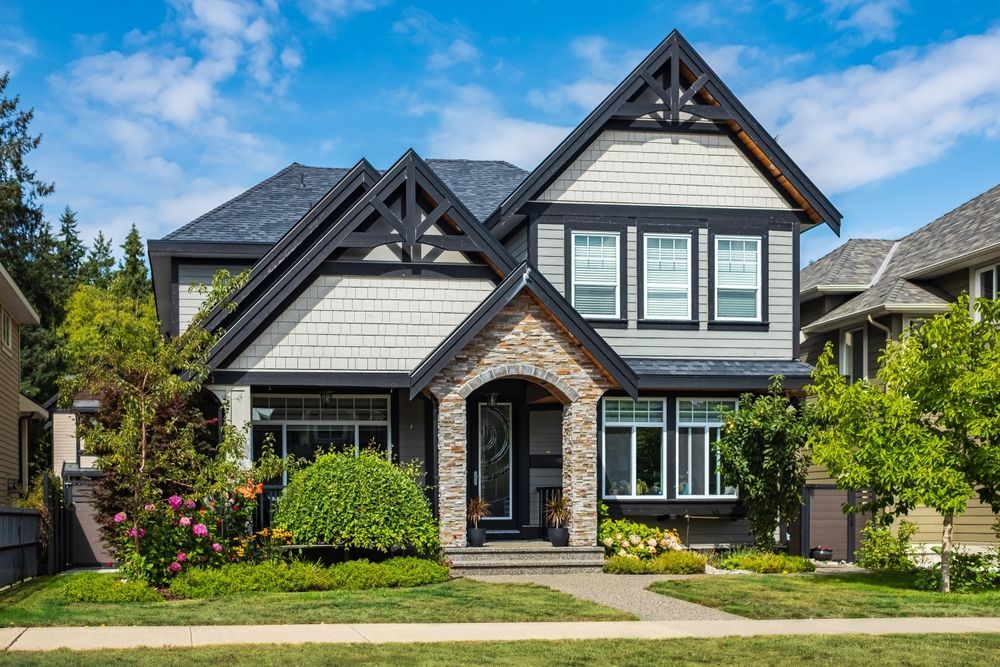 Two-story house with dark gray roof and trim, light gray siding, and stone archway entrance on a sunny day.