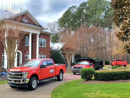 Two red trucks are parked in front of a large brick house.