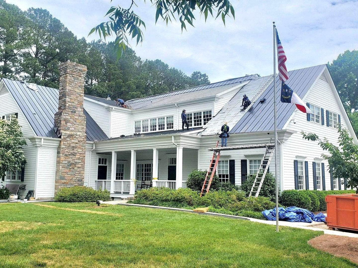 A large white house with a metal roof is being remodeled.