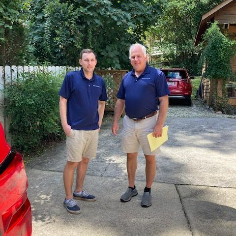 Two men are standing next to each other in a driveway.