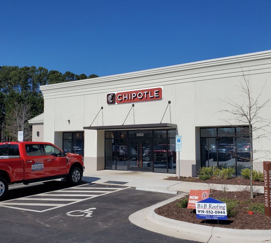 A red truck is parked in front of a chipotle restaurant.