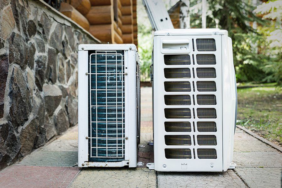 Two air conditioners are sitting next to each other on a sidewalk.