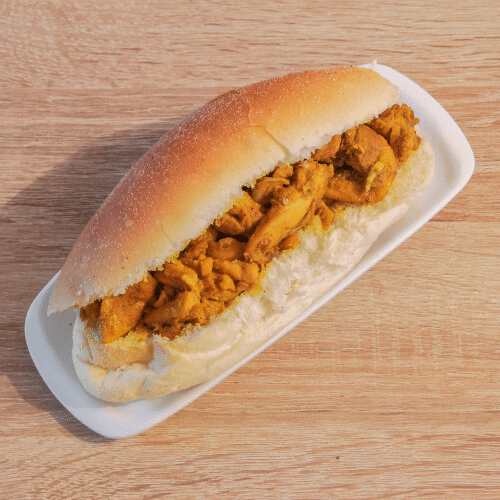 Een broodje kip op een broodje op een witte plaat op een houten tafel.