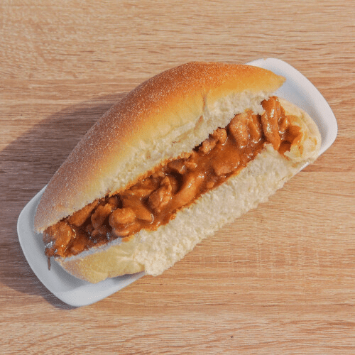 Een broodje kip zit op een wit bord op een houten tafel.