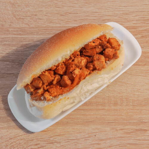 Een broodje kip ligt op een wit bord op een houten tafel.