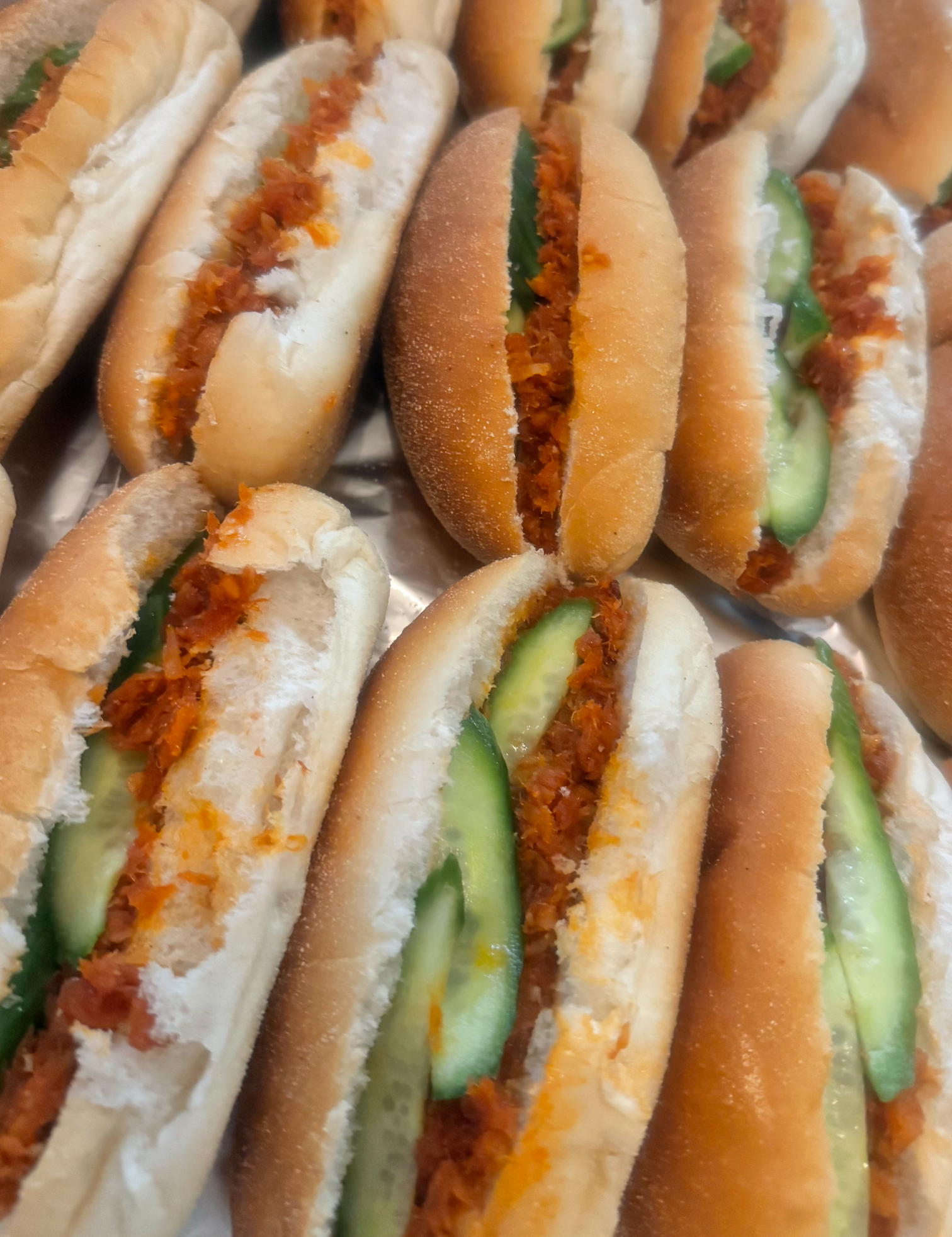 Close-up van een dienblad met sandwiches in zachte broodjes, gevuld met reepjes vlees en plakjes komkommer.