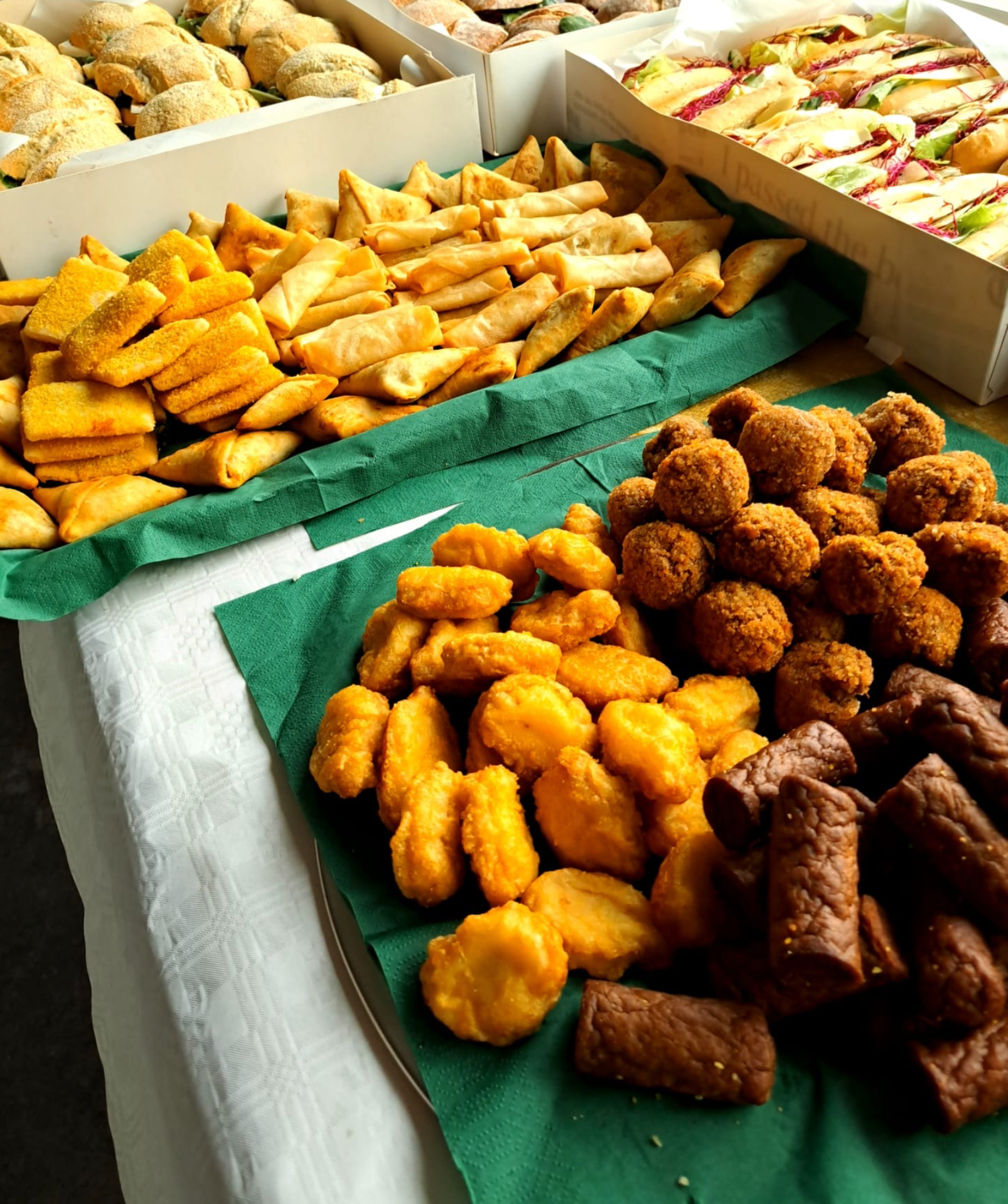 Een buffet met diverse gefrituurde snacks: samosa's, kipnuggets, kroketten en sandwiches.